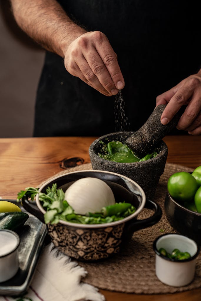 Close-up of hands using a mortar and pestle to prepare Mexican salsa with fresh ingredients.